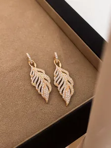 Close-up detail of luxury golden feather drop earrings featuring full cubic zirconia inlay