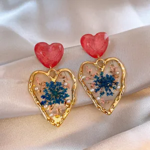 Macro detail of heart earrings with blue dried flowers and pearls in clear resin.