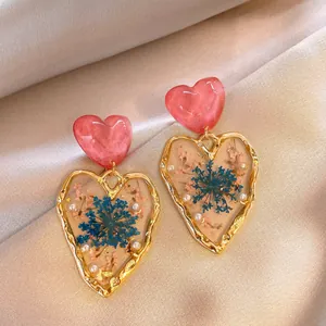 Close-up of handmade resin heart earrings with dried flowers and gold frame details