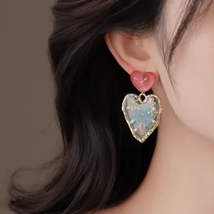 Close-up detail of resin heart earring with blue dried flowers and gold foil inlay