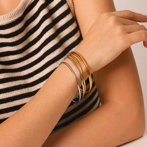 Set of 5 minimalist 18k gold plated stainless steel bangles worn on a female model's wrist