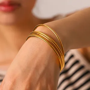 Close-up view of five stacked minimalist 18k gold-plated stainless steel bangles