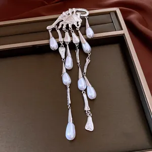 Detailed view of a silver eye brooch with cascading waterdrop pearl tassels on a tray.