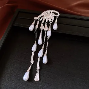 Detail view of a silver eye brooch with elegant pearl teardrop tassels on black tray