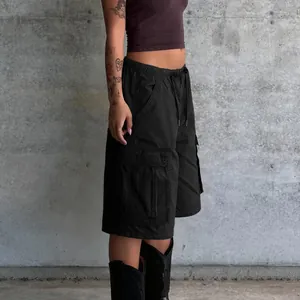 Side detail of black loose cargo shorts with large pockets against a concrete wall.