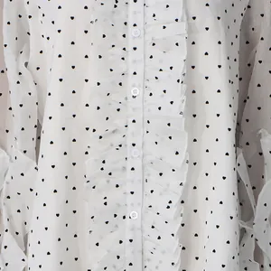 Detail of white blouse featuring black heart patterns and delicate ruffle trim on placket