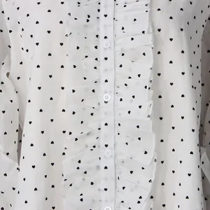 Detailed close-up of ruffle trim and heart pattern on white chiffon long sleeve shirt