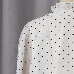 Detail of ruffled stand-up collar and black heart print on white puff sleeve shirt