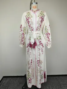 Détail d'une robe longue à fleurs avec une ceinture à la taille et des pompons roses