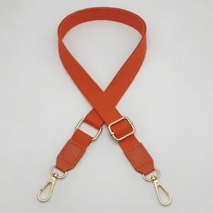 Detail of adjustable cotton shoulder strap with golden metal hooks and orange leather ends