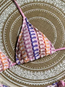 Detailed view of handmade crochet bikini top with colorful wave patterns on straw mat