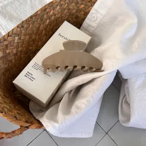 Detail of large khaki acetate hair claw clip placed on white linen fabric inside a basket