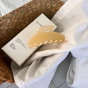 Detail of cream yellow large acetate hair claw clip on white fabric in a woven basket
