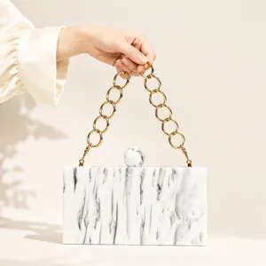 Detail of white marble acrylic evening clutch featuring a gold ring chain handle and clasp