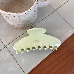 Close-up of light green acetate hair claw clip with gold lettering on a minimalist background
