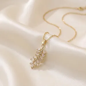Elegante collana a piuma dorata con zirconi su sfondo di seta color champagne
