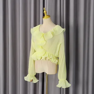 Detail of ruffled edges and vertical pleats on a light yellow long-sleeve blouse