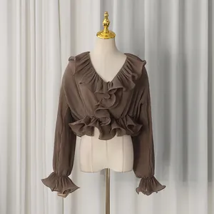 Detail of ruffle trim on brown pleated V-neck shirt showing fabric texture