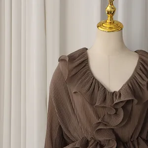 Detailed view of dark brown pleated fabric and ruffled collar on a stylish blouse