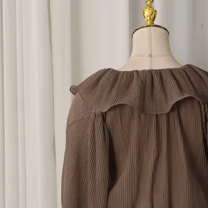 Detailed view of the brown pleated fabric and ruffled collar of the elegant blouse