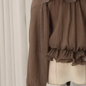 Detail of ruffle hem and pleated texture on dark brown long-sleeved shirt for women