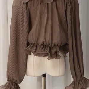 Detail of brown pleated fabric with ruffle hem and sleeve cuffs on a slim fit blouse
