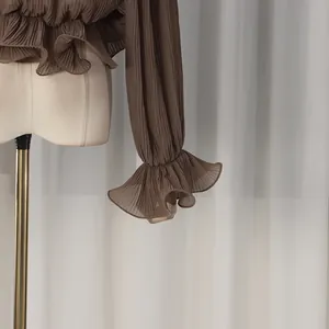 Detail of dark brown pleated shirt featuring elegant ruffle cuffs and textured fabric