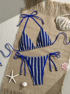 Detailed close-up of a striped knit bikini with gold beads on woven beach mat