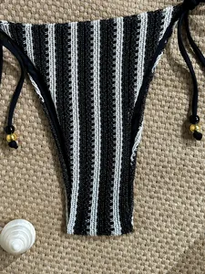 Detail of striped knit bikini bottoms with decorative beads on a beach mat