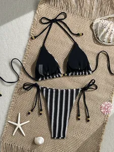 Detail of black knit bikini top with striped waistband and gold beads on straw mat