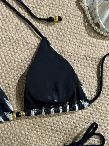 Close-up of black bikini top with crochet trim and beaded tie straps on beige mat