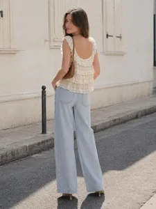 Détail d'un débardeur en dentelle blanche superposée avec un jean bleu clair à jambes larges