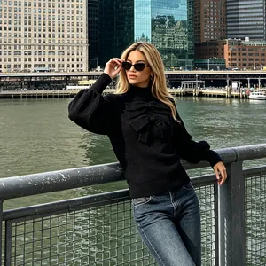Detail of black knit top with a large statement bow and long sleeves in urban setting