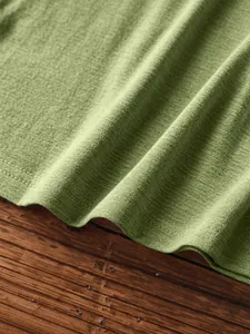 Close-up of grass green knitted fabric texture with double-stitched hem on wood surface
