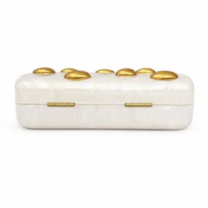 Detail of white marble acrylic evening clutch featuring gold rivet studs and metal hinges