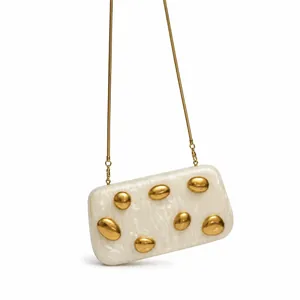 Detail of white marble acrylic clutch with gold pebble accents and snake chain strap