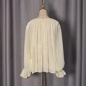 Détail du chemisier plissé crème avec bouton perle au dos et poignets à volants