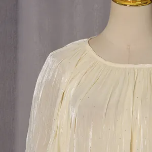 Détail du chemisier crème à manches longues avec texture plissée et accents de strass