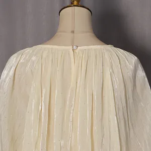 Détail de la blouse plissée champagne avec paillettes et bouton perle au dos de l'encolure