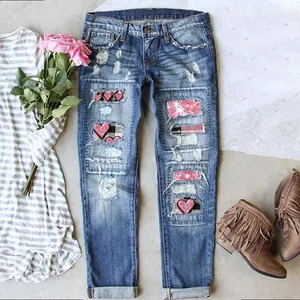 Detail of ripped blue jeans with heart-shaped patches, pink sequins, and boho denim texture