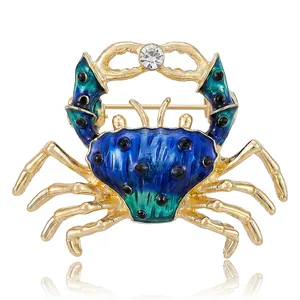 Golden alloy crab brooch with blue enamel and crystal accent on white background