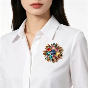Détail d'une broche florale aux cristaux multicolores portée sur un chemisier blanc