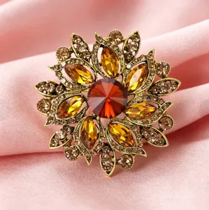 Détail de la broche fleur dorée vintage avec cristaux ambre et rouges sur tissu rose
