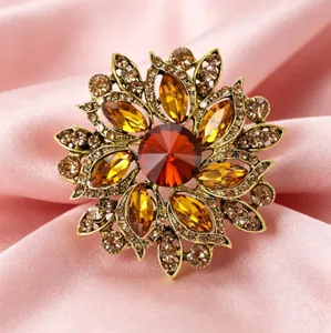 Détail macro d'une broche tournesol rétro dorée aux cristaux colorés sur satin rose