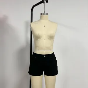 Detail of low-waist black denim shorts with metal button and pocket on a mannequin