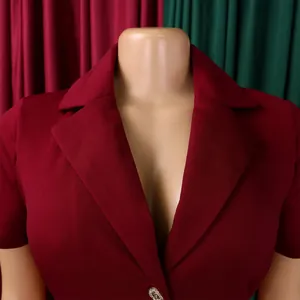 Gros plan du col à revers bordeaux et du bouton métallique texturé sur la robe chic