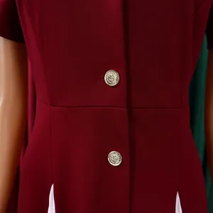 Détail d'une robe bordeaux à manches courtes avec boutons dorés et ourlet plissé blanc