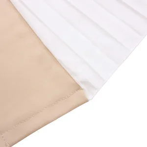 Détail de couture bicolore entre le tissu beige et le textile plissé blanc sur la robe