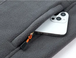 Detail of fleece vest side pocket with orange drawstring zipper holding a smartphone