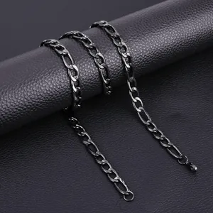 Detail shot of gunmetal Figaro chain necklace draped over black textured surface